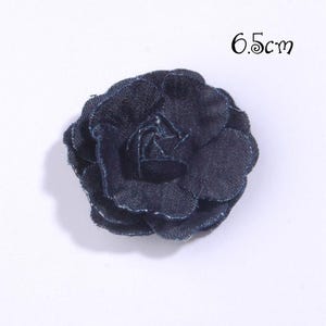 Puede incluir: Una flor de tela vaquera azul oscuro, de 6,5 cm de di&aacute;metro, que se asemeja a una rosa. La flor tiene m&uacute;ltiples p&eacute;talos en capas y un aspecto texturizado. La flor est&aacute; sobre un fondo blanco.