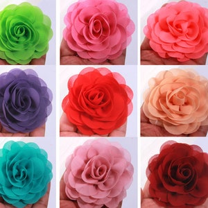 Puede incluir: Surtido de nueve adornos de flores de tela en varios colores, incluyendo verde, rosa, morado, rojo, turquesa, rosa claro y burdeos. Cada flor tiene un diseño en capas y con volantes.