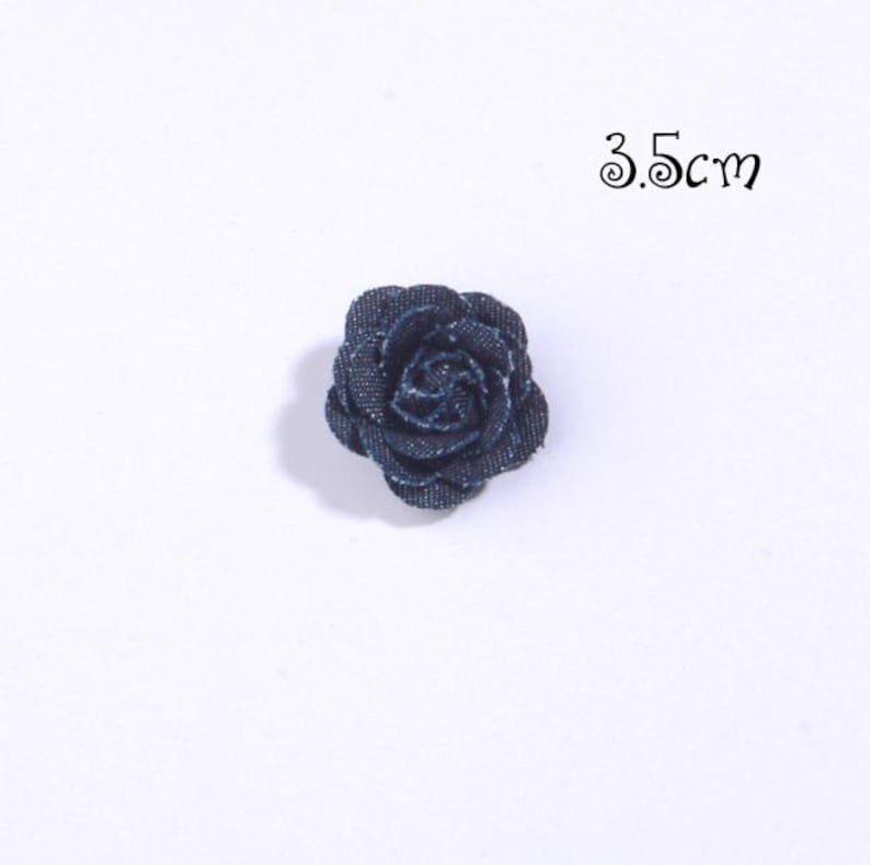 Puede incluir: Una rosa de tela vaquera azul oscuro, de aproximadamente 3,5 cm de di&aacute;metro, sobre un fondo blanco. La flor tiene m&uacute;ltiples capas de p&eacute;talos, creando una apariencia texturizada. Ideal para manualidades y adornos.