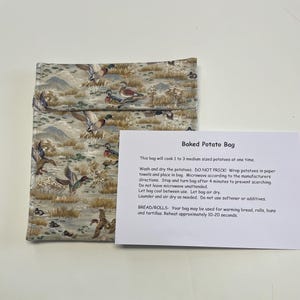 May include: A white cotton bag with a brown and green woodland print featuring ducks and birds. The bag is labeled "Baked Potato Bag" and includes instructions for cooking and reheating potatoes, bread, rolls, and tortillas in the microwave.