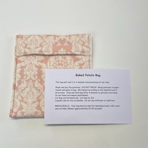 May include: A pink and white patterned fabric bag with instructions for baking potatoes in the microwave. The text reads "Baked Potato Bag" and includes instructions for use and care.  The bag can also be used to warm bread, rolls, buns, and tortillas.