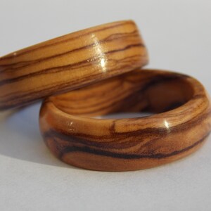 Puede incluir: Dos anillos de madera con un patr&oacute;n de veta de madera natural. Los anillos est&aacute;n apilados uno encima del otro.