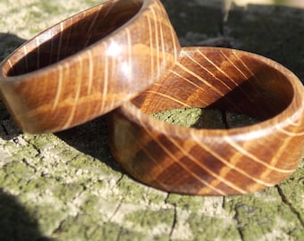 May include: Two wooden rings with a light brown color and a striped pattern. The rings are made of wood and have a smooth finish. The rings are likely handmade and are a unique accessory.