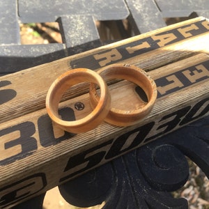May include: Two wooden rings with a light brown color are displayed on top of two hockey sticks. The rings have a smooth, polished finish. The hockey sticks are light brown with black text and markings.