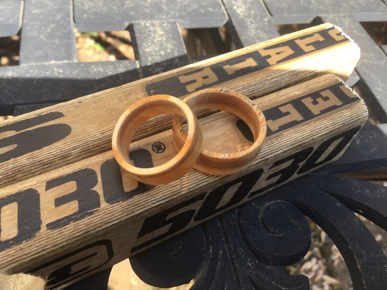 May include: Two wooden rings with a light brown color are displayed on top of two hockey sticks. The rings have a smooth, polished finish. The hockey sticks are light brown with black text and markings.