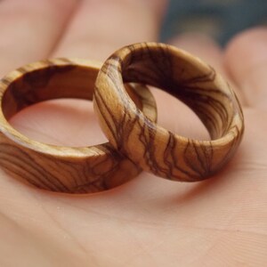 Puede incluir: Dos anillos de madera con un patr&oacute;n de veta de madera natural. Los anillos est&aacute;n hechos de madera marr&oacute;n claro con vetas marr&oacute;n oscuro.