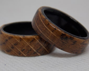 May include: Two wooden rings with a black interior. The rings have a brown wood grain pattern with black accents.