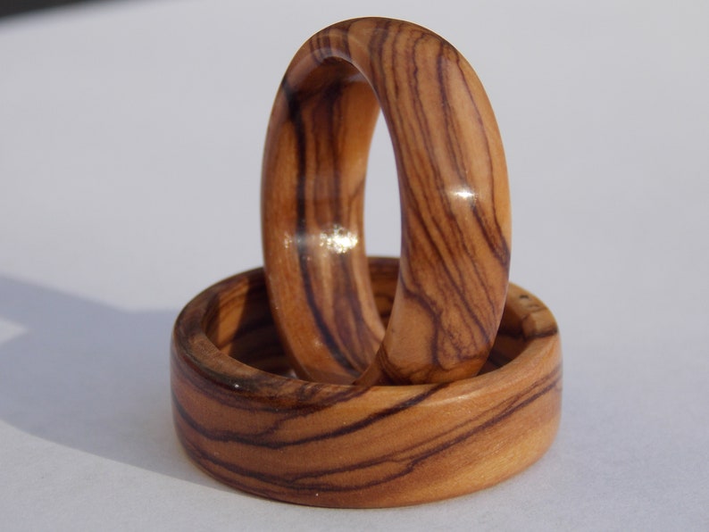 Puede incluir: Dos anillos de madera con un patr&oacute;n de veta de madera natural. Los anillos est&aacute;n apilados uno encima del otro.