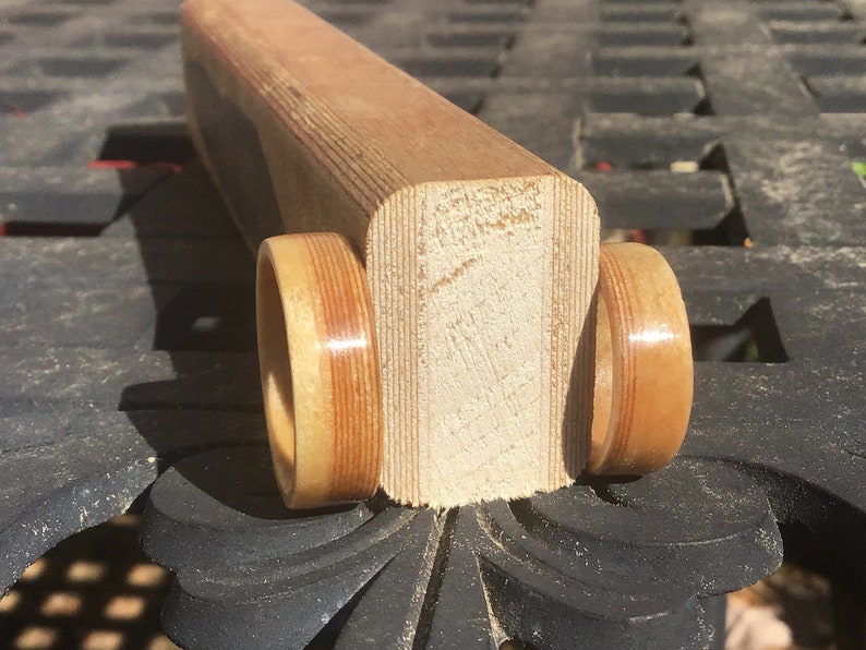 May include: A wooden toy car with two wheels and a rectangular body. The wheels and body are made of light brown wood with darker brown stripes. The toy is sitting on a dark surface.