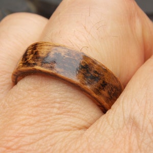 K&ouml;nnte beinhalten: Nahaufnahme eines Holzrings mit einer dunkelbraunen Beize und einer gl&auml;nzenden Oberfl&auml;che. Der Ring wird an einem Finger getragen.