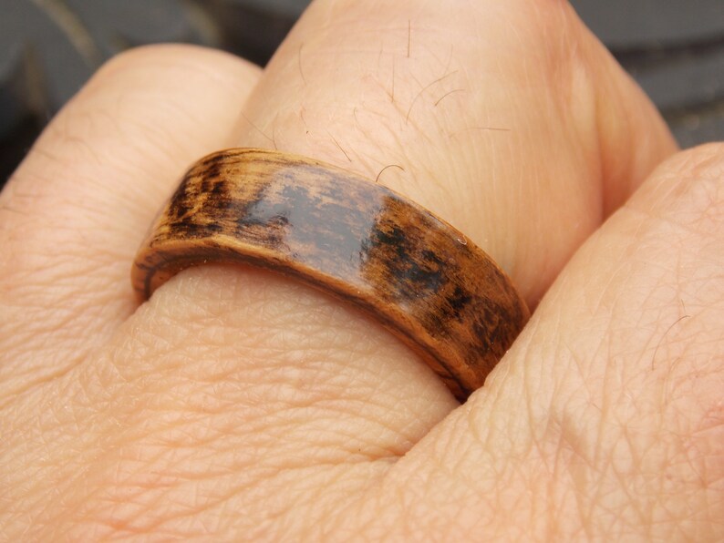 K&ouml;nnte beinhalten: Nahaufnahme eines Holzrings mit einer dunkelbraunen Beize und einer gl&auml;nzenden Oberfl&auml;che. Der Ring wird an einem Finger getragen.