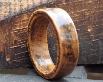 May include: A wooden ring with a dark brown stain and a natural wood grain. The ring is smooth and polished.