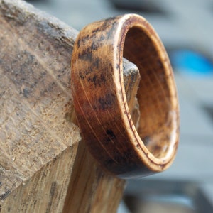 K&ouml;nnte beinhalten: Nahaufnahme eines Holzrings mit einer dunkelbraunen Beize. Der Ring besteht aus mehreren Holzschichten, und die Maserung ist sichtbar. Der Ring liegt auf einem St&uuml;ck Holz.
