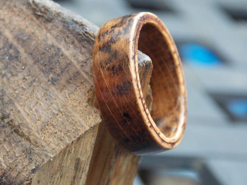 K&ouml;nnte beinhalten: Nahaufnahme eines Holzrings mit einer dunkelbraunen Beize. Der Ring besteht aus mehreren Holzschichten, und die Maserung ist sichtbar. Der Ring liegt auf einem St&uuml;ck Holz.