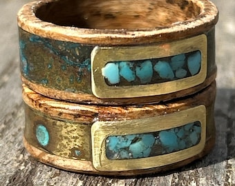 May include: Two stacked rings featuring a wooden band base with inlaid metal sections. The metal components include a rectangular brass inlay filled with crushed turquoise stone fragments and a weathered copper-toned surface with green patina.