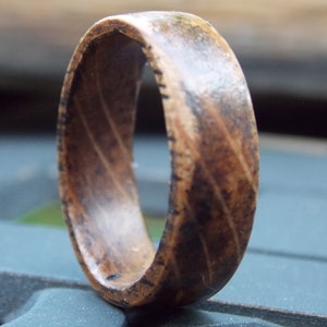 K&ouml;nnte beinhalten: Ein Holzring mit einem Muster aus dunkelbraunem und hellbraunem Holz. Der Ring besteht aus einem einzigen St&uuml;ck Holz und hat eine glatte, polierte Oberfl&auml;che.