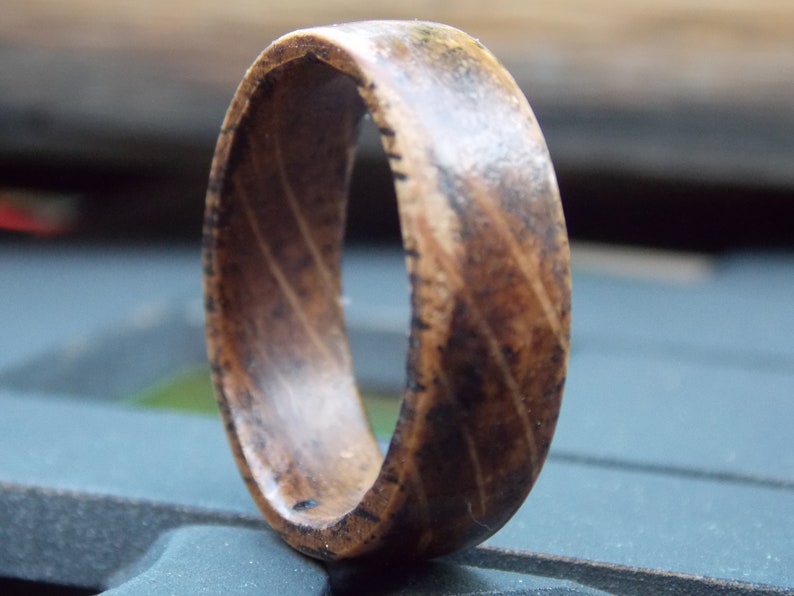 K&ouml;nnte beinhalten: Ein Holzring mit einem Muster aus dunkelbraunem und hellbraunem Holz. Der Ring besteht aus einem einzigen St&uuml;ck Holz und hat eine glatte, polierte Oberfl&auml;che.