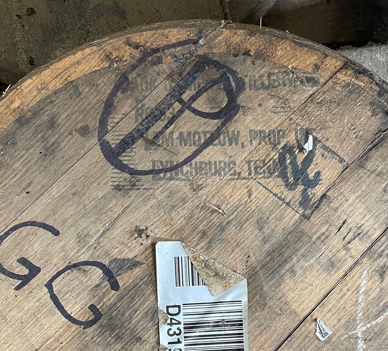 K&ouml;nnte beinhalten: Nahaufnahme eines Holzfasses mit schwarzen Markierungen. Das Fass hat ein Etikett mit dem Text "D431" und einem Barcode. Der Text "Jim Motow, Prop.  Exchequer, Tex." ist auf dem Fass sichtbar.
