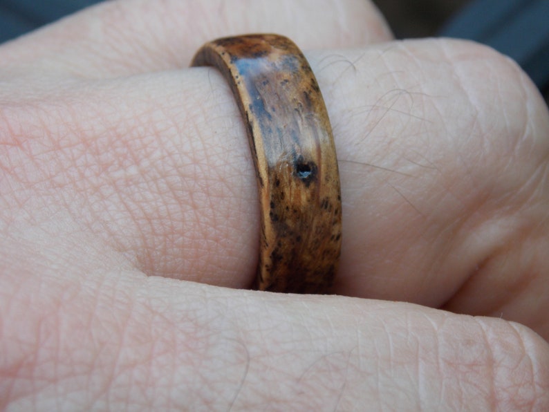 K&ouml;nnte beinhalten: Nahaufnahme eines Holzrings mit einer dunkelbraunen Beize. Der Ring wird an einem Finger getragen.