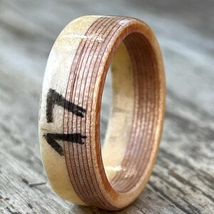 May include: A wooden ring with a light beige exterior and a dark brown interior band. The number "17" is painted in black on the ring's exterior. The ring is made of layered wood and has a smooth finish.