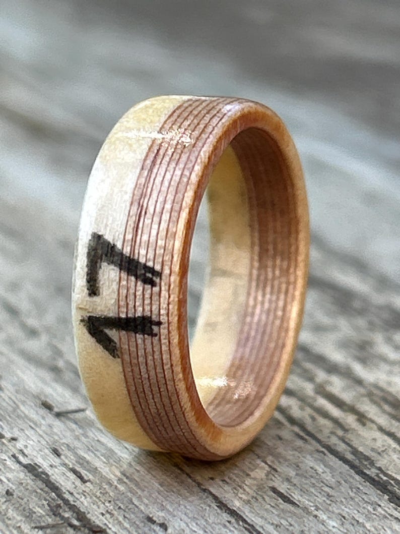 May include: A wooden ring with a light beige exterior and a dark brown interior band. The number "17" is painted in black on the ring's exterior. The ring is made of layered wood and has a smooth finish.