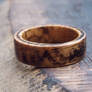 K&ouml;nnte beinhalten: Ein dunkelbrauner Holzring mit einem helleren Holzmaserungsmuster. Der Ring hat eine glatte, polierte Oberfl&auml;che.