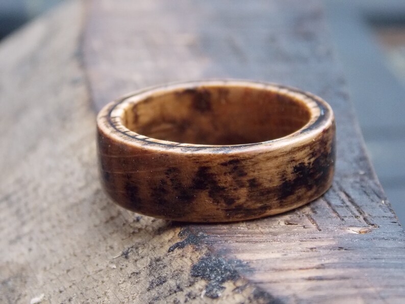 K&ouml;nnte beinhalten: Ein dunkelbrauner Holzring mit einem helleren Holzmaserungsmuster. Der Ring hat eine glatte, polierte Oberfl&auml;che.