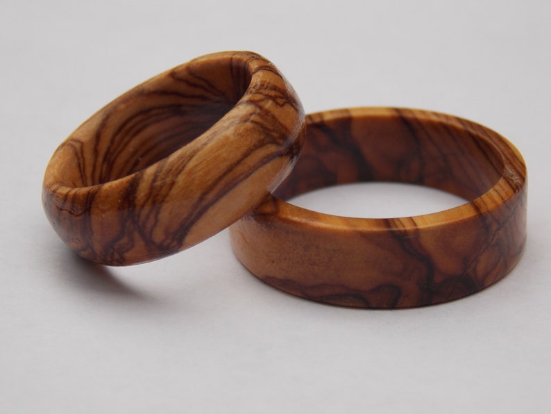Puede incluir: Dos anillos de madera hechos de madera de olivo. Los anillos tienen un color marr&oacute;n natural con patrones de grano marr&oacute;n oscuro.