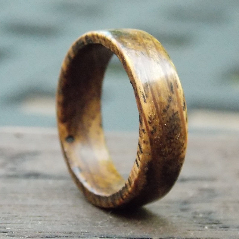 K&ouml;nnte beinhalten: Ein Holzring mit einem Muster aus dunkelbraunem und hellbraunem Holz. Der Ring ist poliert und hat eine glatte Oberfl&auml;che.