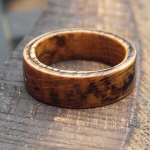 K&ouml;nnte beinhalten: Ein Holzring mit dunkelbrauner Oberfl&auml;che. Der Ring hat ein breites Band und eine glatte Oberfl&auml;che.
