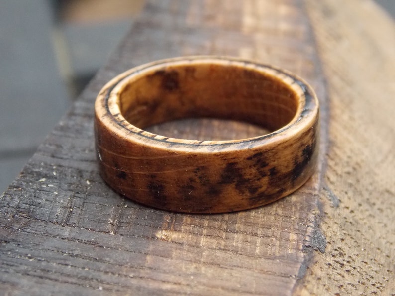 K&ouml;nnte beinhalten: Ein Holzring mit dunkelbrauner Oberfl&auml;che. Der Ring hat ein breites Band und eine glatte Oberfl&auml;che.
