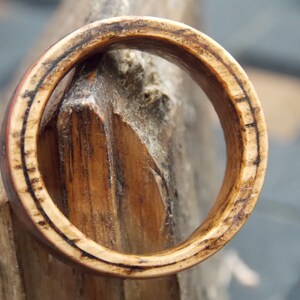 K&ouml;nnte beinhalten: Nahaufnahme eines Holzrings mit dunkelbrauner Oberfl&auml;che. Der Ring besteht aus mehreren Holzschichten, die ein einzigartiges Muster bilden.