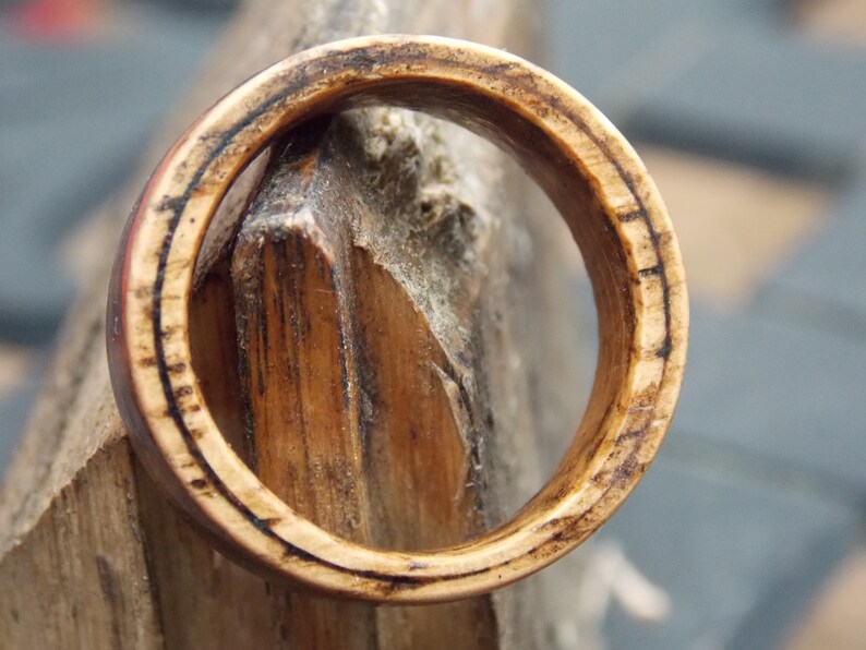 K&ouml;nnte beinhalten: Nahaufnahme eines Holzrings mit dunkelbrauner Oberfl&auml;che. Der Ring besteht aus mehreren Holzschichten, die ein einzigartiges Muster bilden.