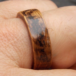 K&ouml;nnte beinhalten: Ein dunkelbrauner Holzring mit gl&auml;nzender Oberfl&auml;che. Der Ring wird an einem Finger getragen.