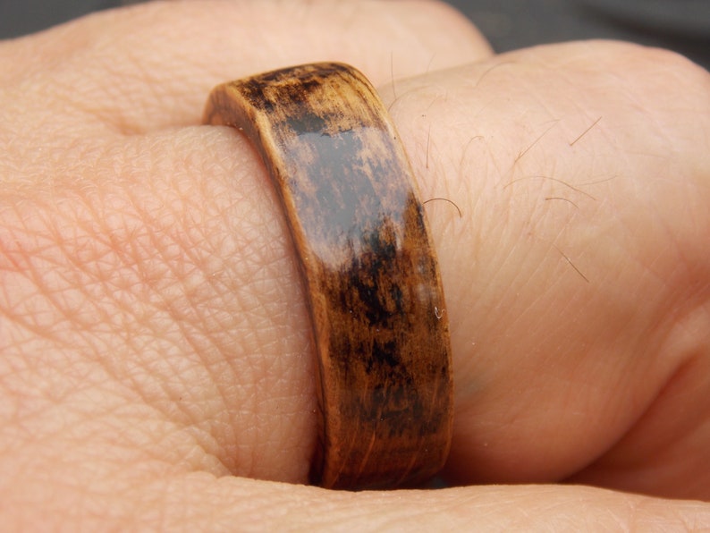 K&ouml;nnte beinhalten: Ein dunkelbrauner Holzring mit gl&auml;nzender Oberfl&auml;che. Der Ring wird an einem Finger getragen.