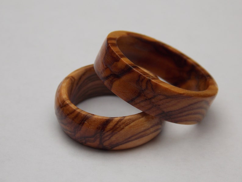 Puede incluir: Dos anillos de madera hechos de madera de olivo. Los anillos est&aacute;n apilados uno encima del otro. La veta de la madera es visible en los anillos.