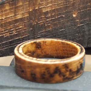 K&ouml;nnte beinhalten: Ein Holzring mit dunkelbrauner Oberfl&auml;che. Der Ring hat ein nat&uuml;rliches Holzmaserungsmuster und eine glatte, polierte Oberfl&auml;che.