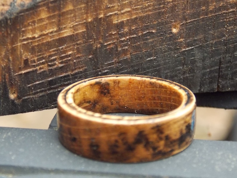 K&ouml;nnte beinhalten: Ein Holzring mit dunkelbrauner Oberfl&auml;che. Der Ring hat ein nat&uuml;rliches Holzmaserungsmuster und eine glatte, polierte Oberfl&auml;che.