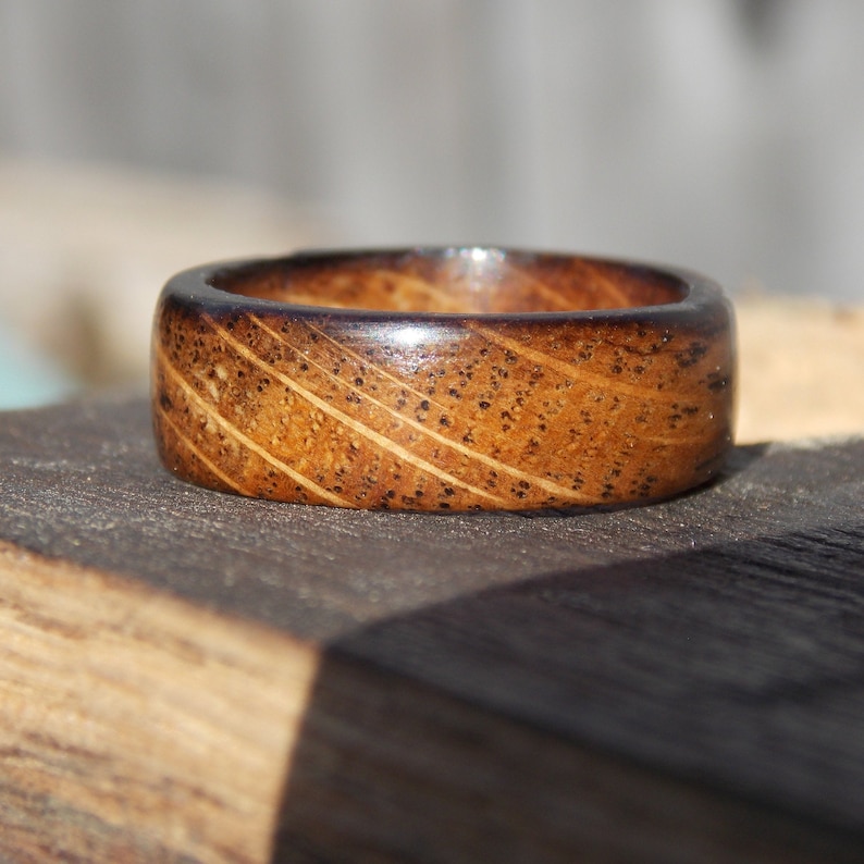 K&ouml;nnte beinhalten: Ein Holzring mit dunkelbrauner Oberfl&auml;che und einem hellbraunen Holzmaserungsmuster. Der Ring hat eine glatte, polierte Oberfl&auml;che.
