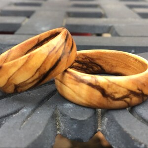 Puede incluir: Dos anillos de madera con un patr&oacute;n de veta de madera natural y vetas marrones oscuras. Los anillos est&aacute;n apilados uno encima del otro.