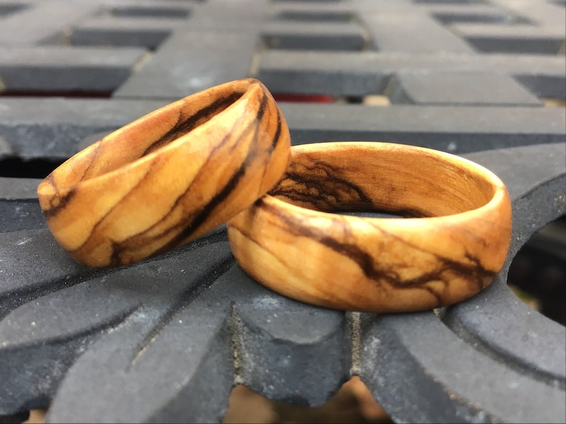 Puede incluir: Dos anillos de madera con un patr&oacute;n de veta de madera natural y vetas marrones oscuras. Los anillos est&aacute;n apilados uno encima del otro.