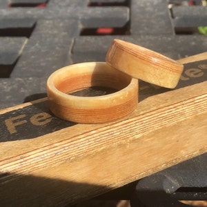 May include: Two wooden rings with a layered design. The rings are light brown with reddish-brown stripes. One ring is larger than the other. The rings are on a wooden surface.
