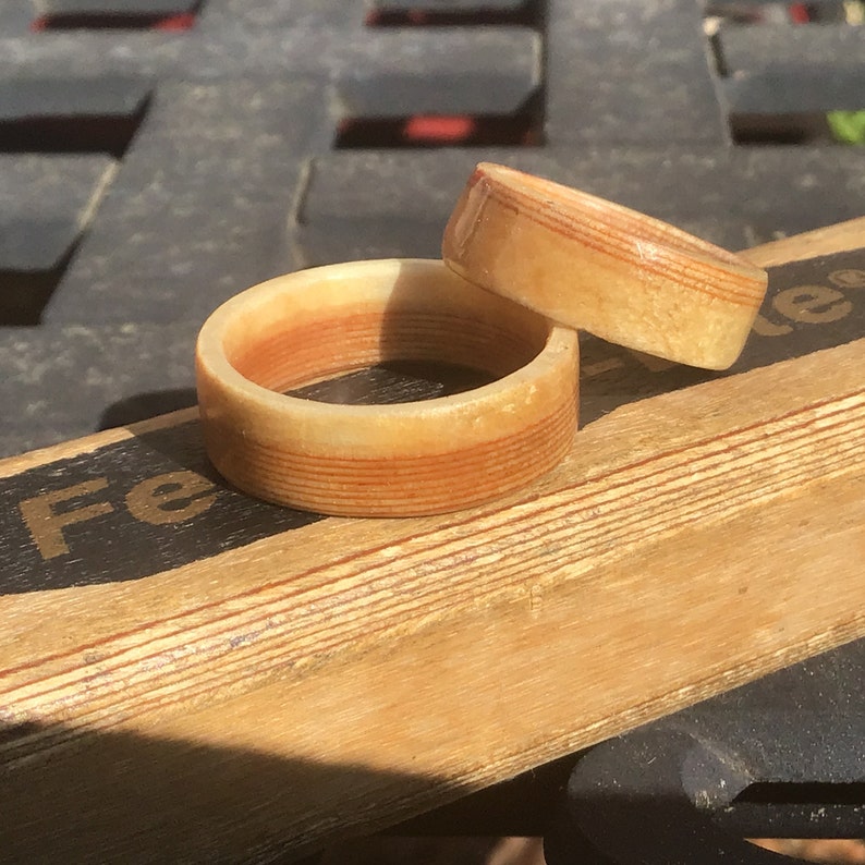 May include: Two wooden rings with a layered design. The rings are light brown with reddish-brown stripes. One ring is larger than the other. The rings are on a wooden surface.