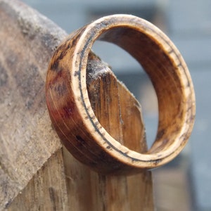 K&ouml;nnte beinhalten: Ein Holzring mit nat&uuml;rlicher brauner Oberfl&auml;che. Der Ring hat ein breites Band und eine glatte, polierte Oberfl&auml;che.