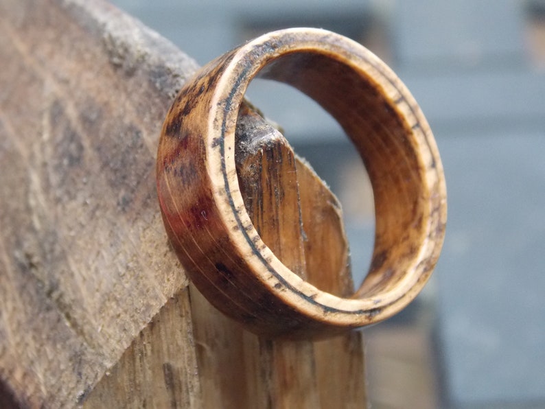 K&ouml;nnte beinhalten: Ein Holzring mit nat&uuml;rlicher brauner Oberfl&auml;che. Der Ring hat ein breites Band und eine glatte, polierte Oberfl&auml;che.