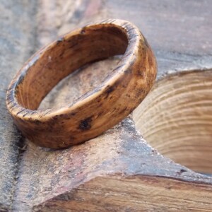 K&ouml;nnte beinhalten: Ein Holzring mit nat&uuml;rlicher brauner Oberfl&auml;che. Der Ring hat ein breites Band und eine glatte, abgerundete Oberfl&auml;che.