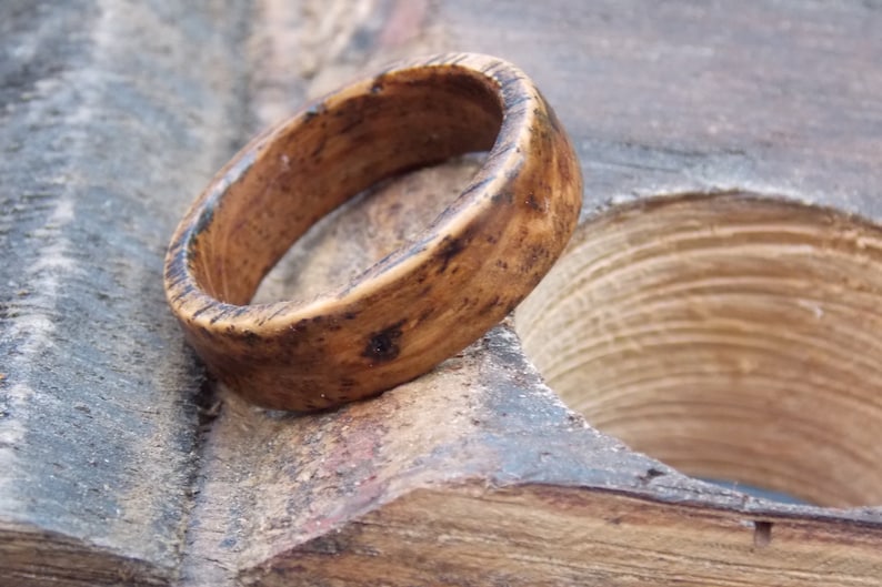 K&ouml;nnte beinhalten: Ein Holzring mit nat&uuml;rlicher brauner Oberfl&auml;che. Der Ring hat ein breites Band und eine glatte, abgerundete Oberfl&auml;che.