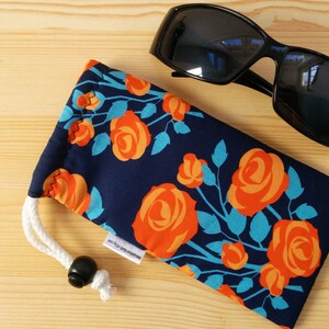 May include: A navy blue eyeglass case with a floral pattern of orange roses and turquoise leaves. The case has a white drawstring and a black toggle.