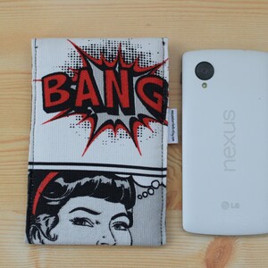 Pu&ograve; includere: Una custodia per telefono bianca con un design in stile fumetto che presenta una grafica "BANG" rossa e nera e un'illustrazione in bianco e nero di una donna. La custodia &egrave; accanto a un telefono Nexus bianco.
