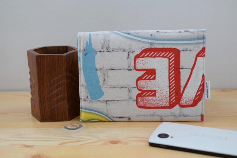 K&ouml;nnte beinhalten: Eine wei&szlig;e Stofftasche mit einem Ziegelmauermuster und roter und blauer Graffiti-Beschriftung, die "Love" sagt.